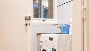Een kleine wasruimte met een voorlader wasmachine, een klein raam en een betegelde spatwand.