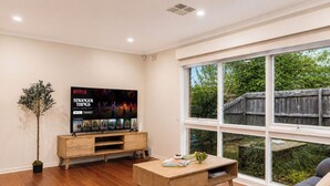 Een moderne woonkamer met een grote televisie, houten meubels en uitzicht op het groen.