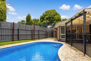 A backyard with a swimming pool, a covered patio, and a wooden fence. - Wantirna 4BR Family Home | Space for Longer Stays (Wantirna South)