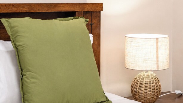 Een hotelkamer met een bed, een groen kussen, een nachtkastje met een lamp en twee aan de muur gehangen schilderijen.