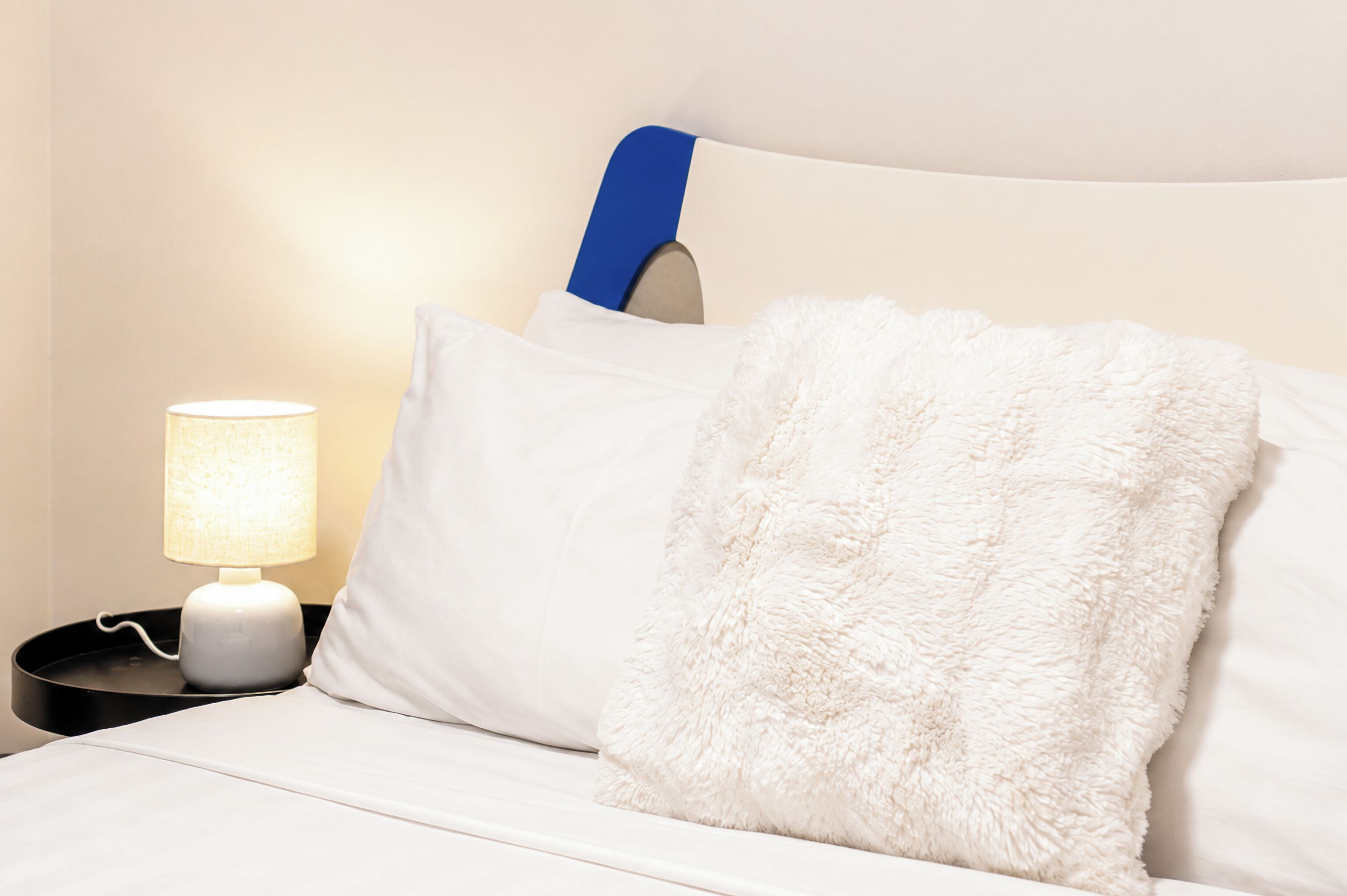 Un letto con biancheria da letto bianca e un cuscino soffice, una lampada da comodino e una testiera blu.