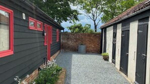 En innergård med en grusgång, en tegelmur och två byggnader med röda fönsterramar och svarta dörrar.