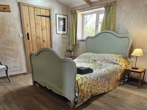 Une chambre à coucher avec un lit, une fenêtre avec des rideaux, une table de chevet avec une lampe et une porte.