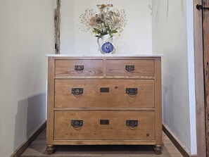 Eine Holzkommode mit Metallgriffen und einer Vase mit getrockneten Blumen darauf.