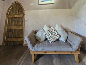 Ein Zimmer mit Holztür, einem grauen Sofa mit gemusterten Kissen und einem gerahmten Bild an der Wand.