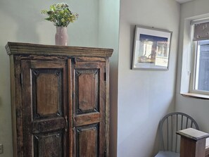 Ein Holzschrank mit Blumen in einer Vase darauf, ein gerahmtes Bild an der Wand und ein Fenster mit Blick.