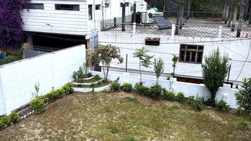 Un edificio de varios pisos con techo plano, rodeado de árboles y una zona cercada.