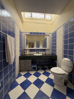 A bathroom with blue and white checkered floor tiles, a white toilet, a sink with a mirror above it, and a towel hanging on the wall. - 3 + 1 BR Villa with lawn, fireplace, foosball & mountain view. (Naina Range)