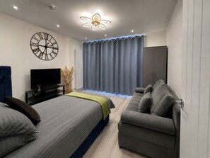 Ein modernes Schlafzimmer mit Bett, Sofa, Fernseher, einer Zieruhr und einer Deckenleuchte.