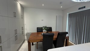 A modern dining area with a wooden table, black chairs, and a potted plant. - House Sleeps 9 with Wifi (Slough)