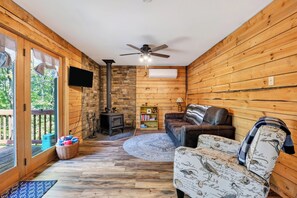 Ein gemütliches Blockhauss-Interieur mit Kamin, einer Couch, einem Fernseher und einem Deckenventilator.
