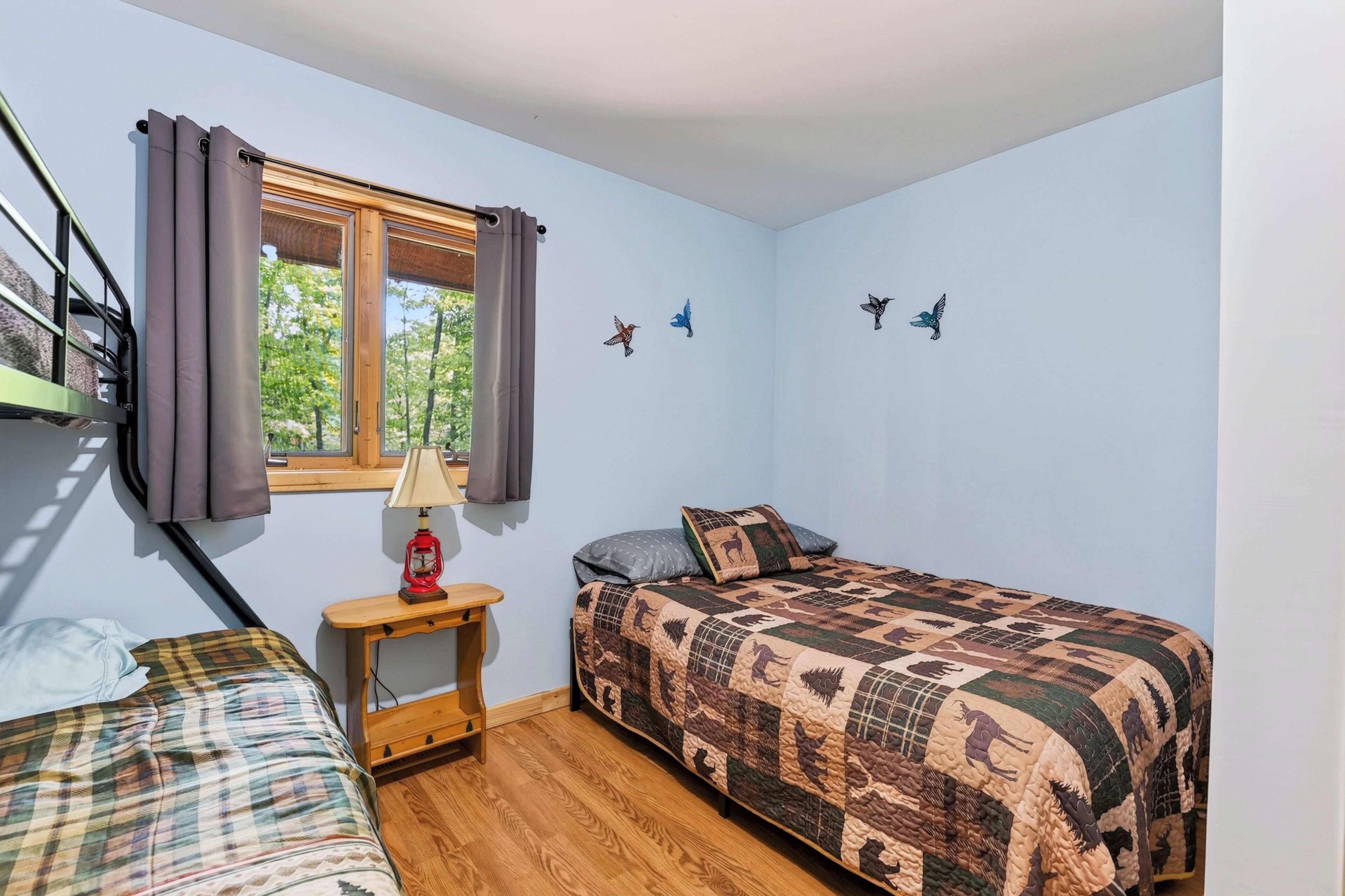 Un dormitorio con dos camas, una ventana con cortinas, una lámpara de noche y adhesivos de pájaros en la pared.