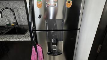 Frigorifero in acciaio inox con erogatore d'acqua, due calamite e un asciugamano rosa appeso alla maniglia.
