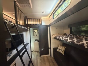 A compact room with bunk beds, a small kitchenette, and a window with a view. - Happy Camper FamilY Fifth Wheel Ultimate Camping Experience DELIVERY+SETUP (Arlington)