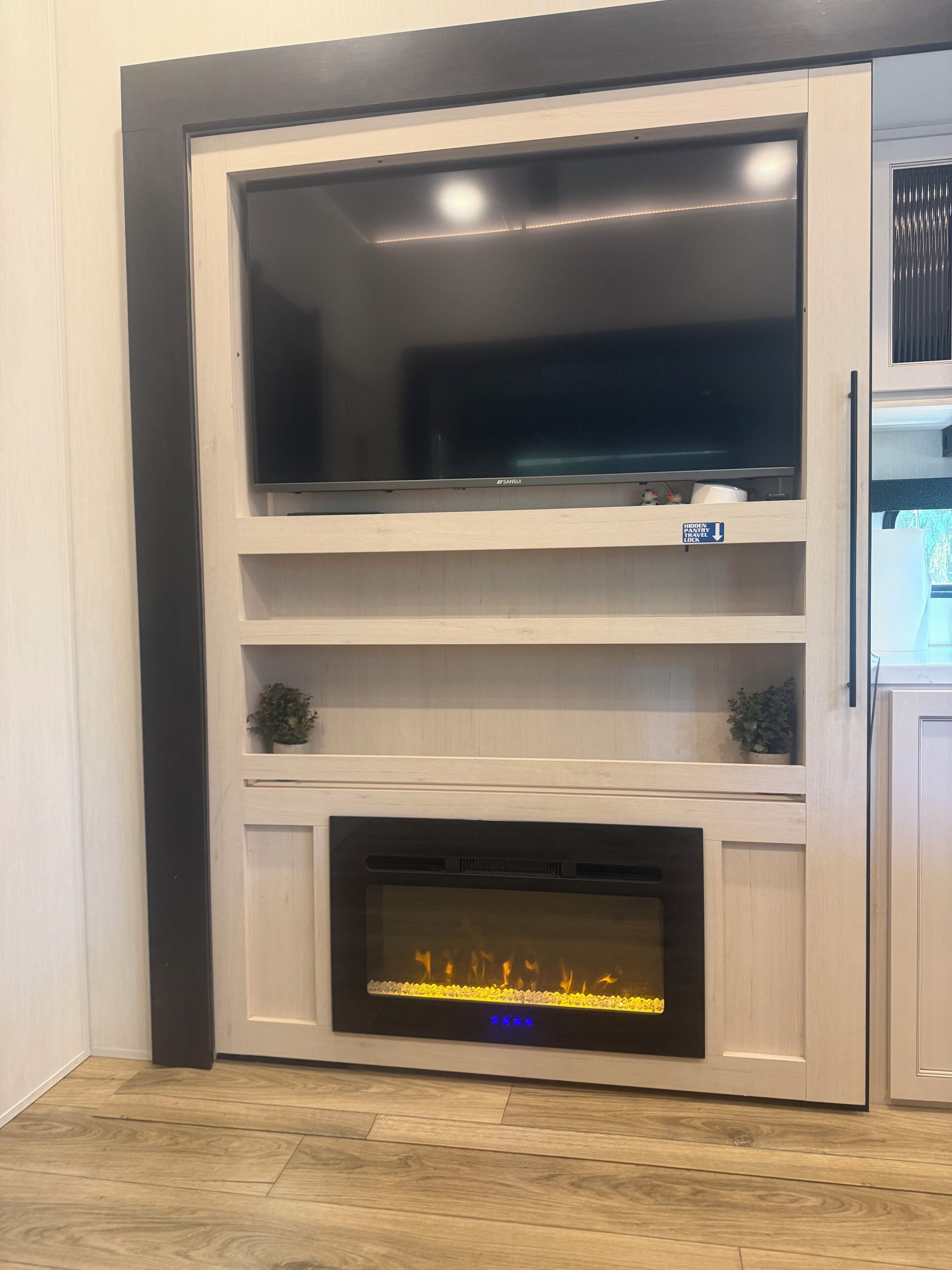 A modern entertainment unit with a flat-screen TV, a fireplace, and a small shelf.