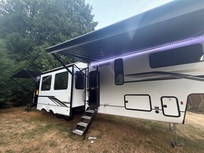 Een witte camper met een overdekte veranda en een ladder naar de ingang.