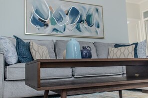 Ein Wohnzimmer mit einem grauen Sofa, einem Holztisch und einer blauen Vase.