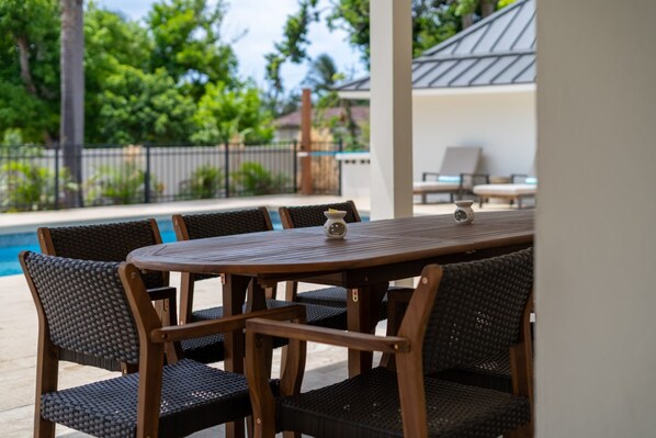 A covered outdoor dining area with a pool in the background.