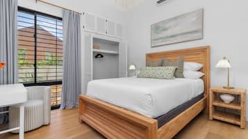 A bedroom with a wooden bed, a desk, and a chair. There is a window with blinds, an air conditioning unit, and a painting on the wall.