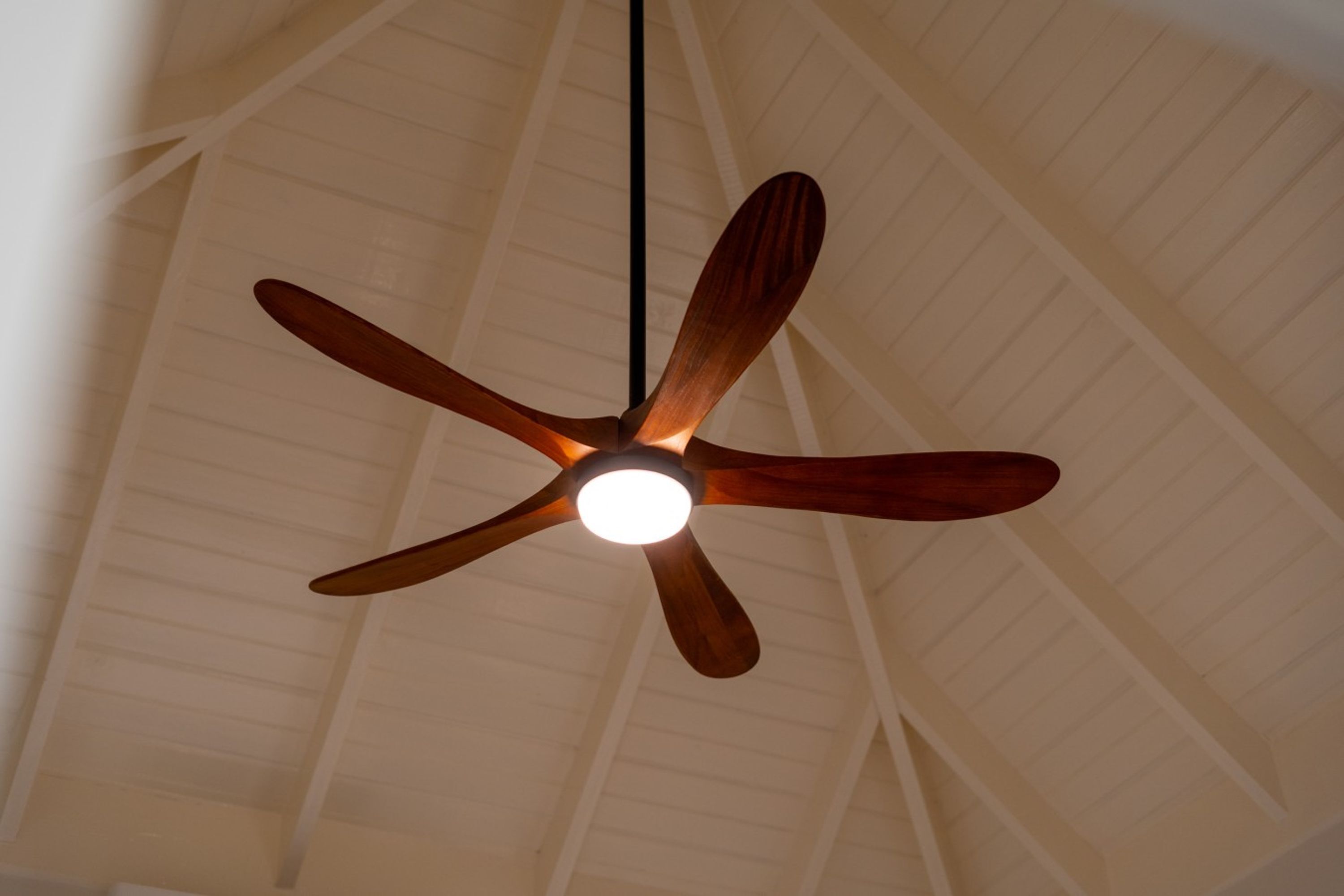 A ceiling fan with a wooden design and a light fixture in a room with a high, sloped ceiling.