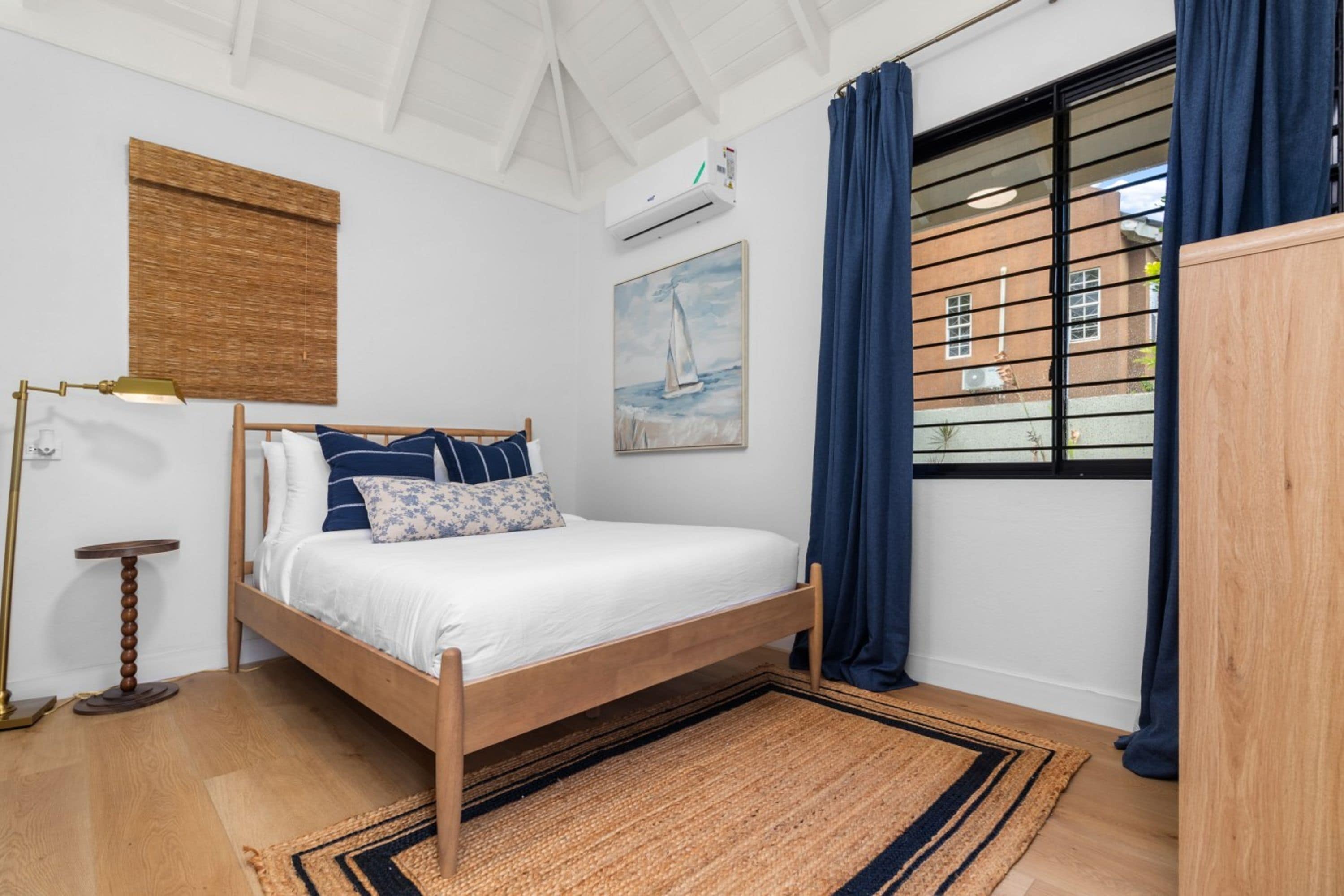 A bedroom with a wooden bed, a bedside lamp, a rug, a painting, and a window with curtains.