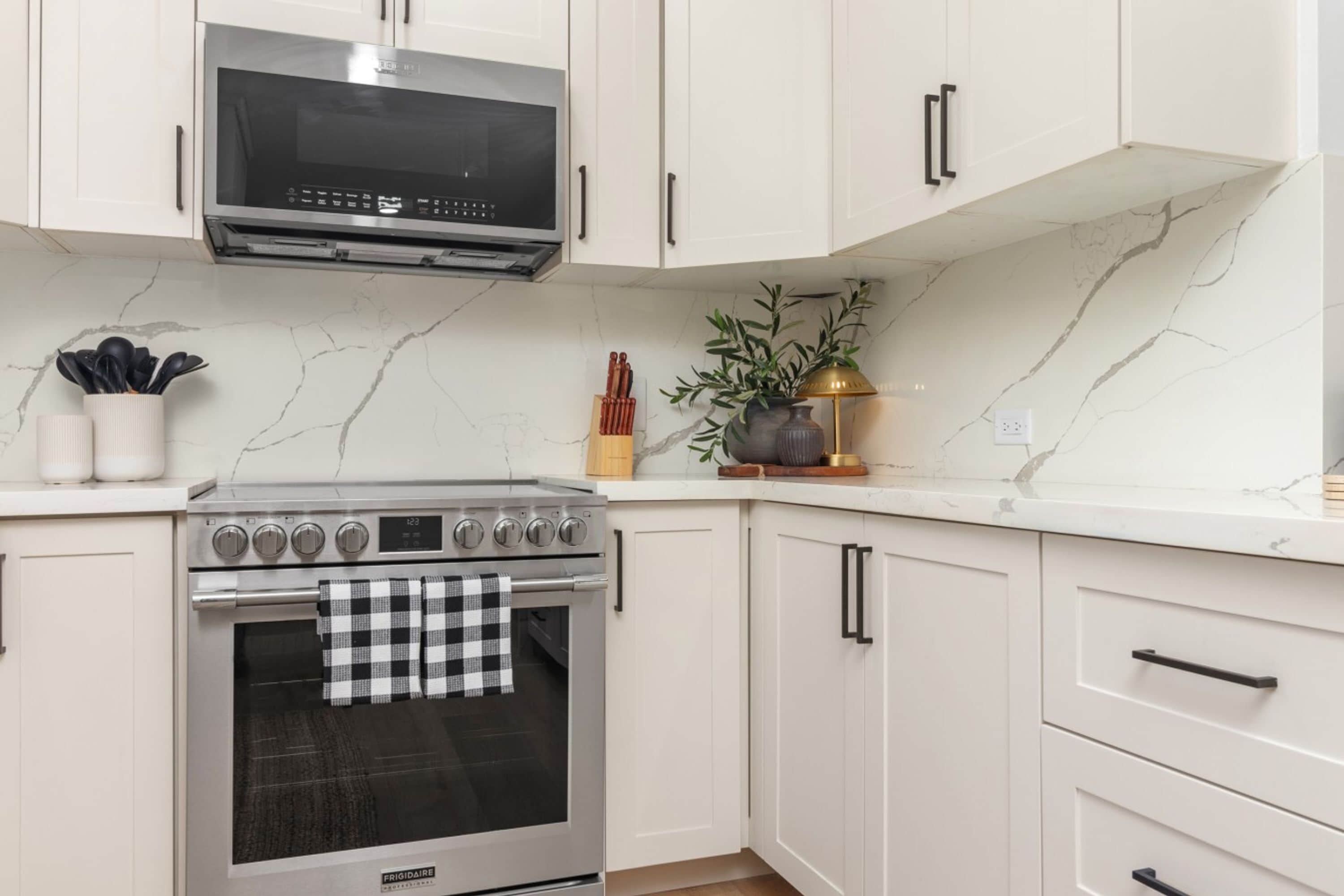 Una cocina con armarios blancos, horno de acero inoxidable y microondas.
