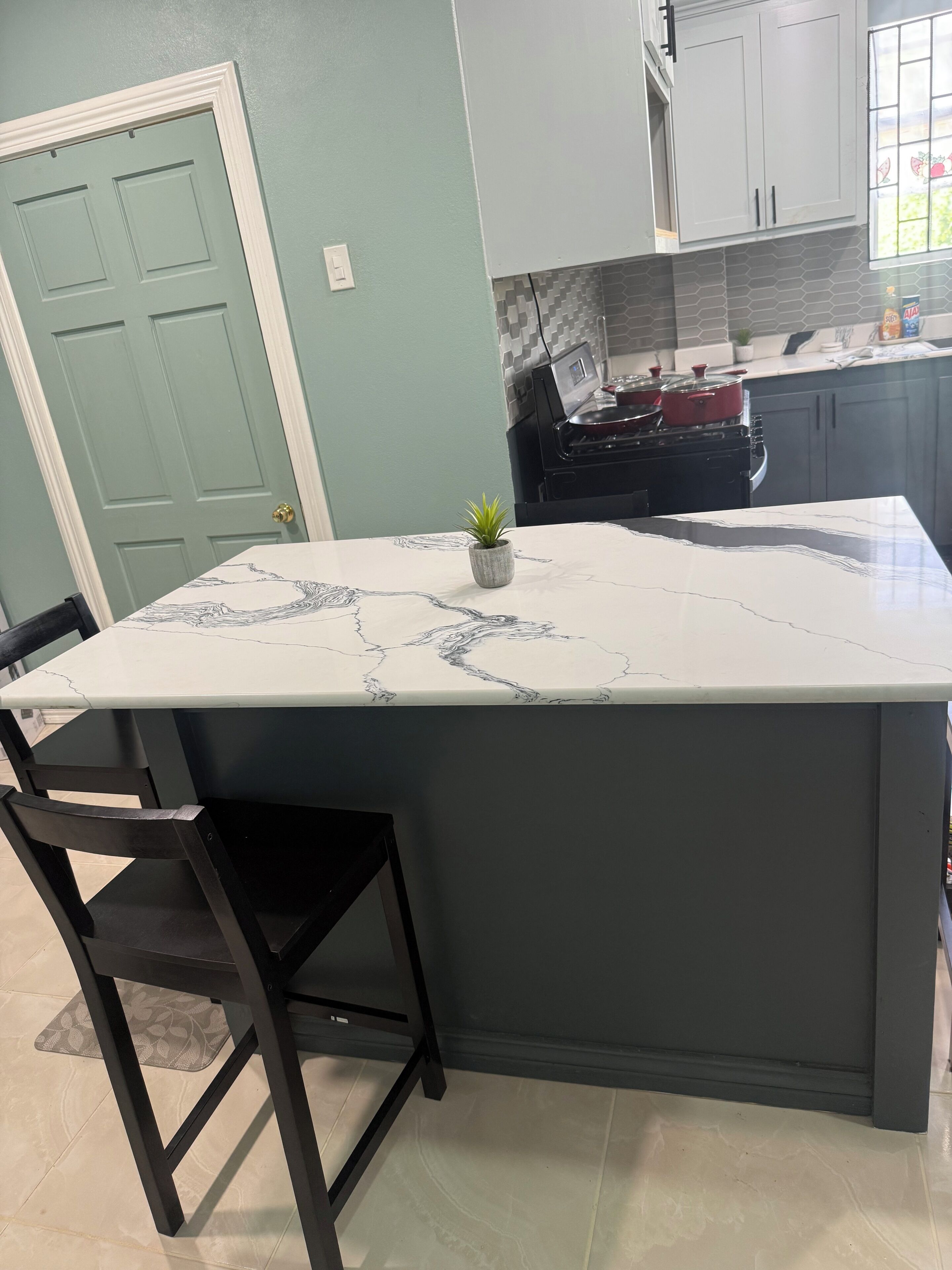 A kitchen with a marble countertop island, a small potted plant, and a stove.