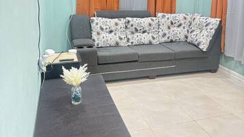A living room with a grey sofa, a black entertainment unit, and a vase with white flowers.