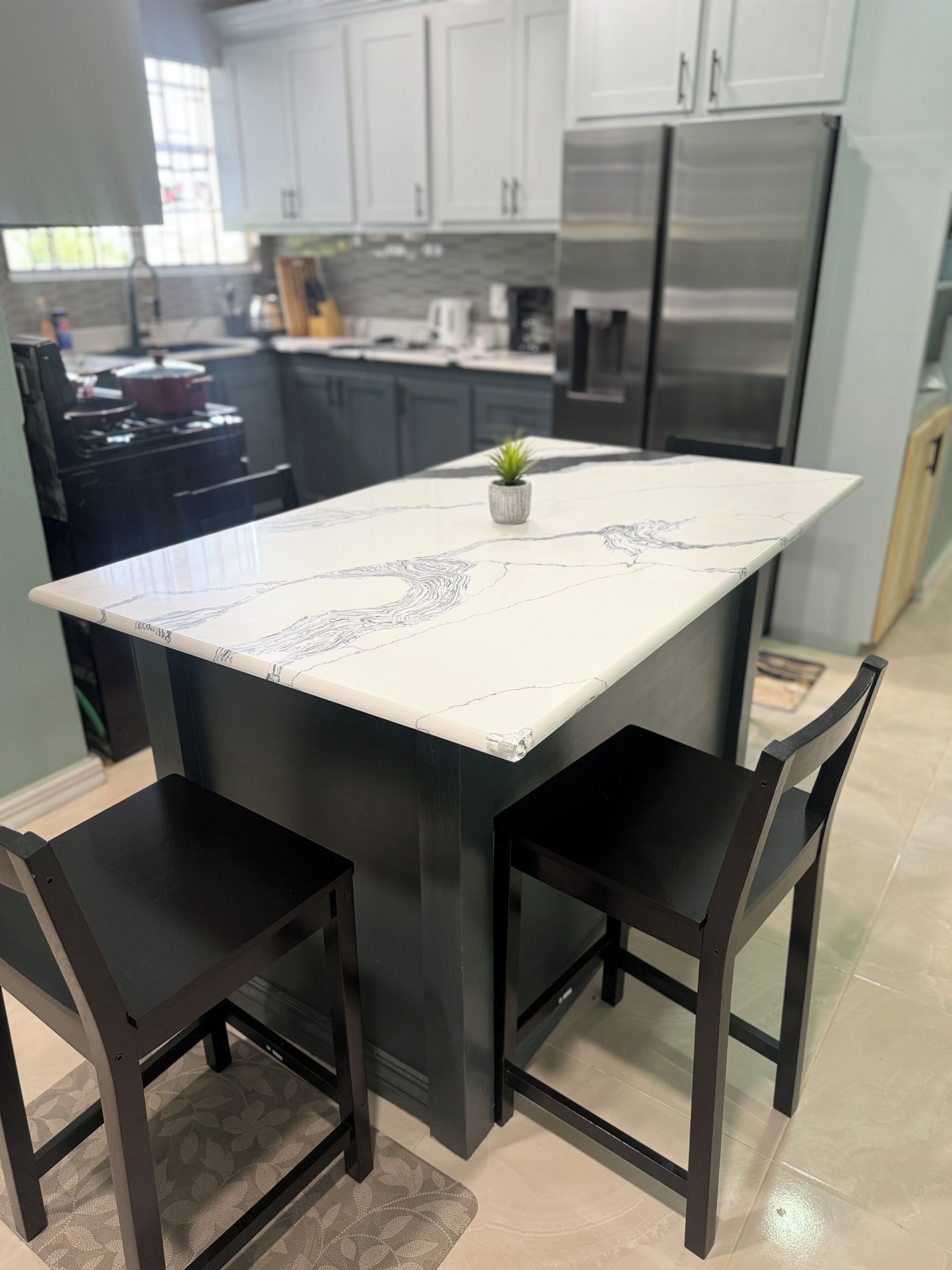 A kitchen with a central island, dark chairs, and a potted plant.