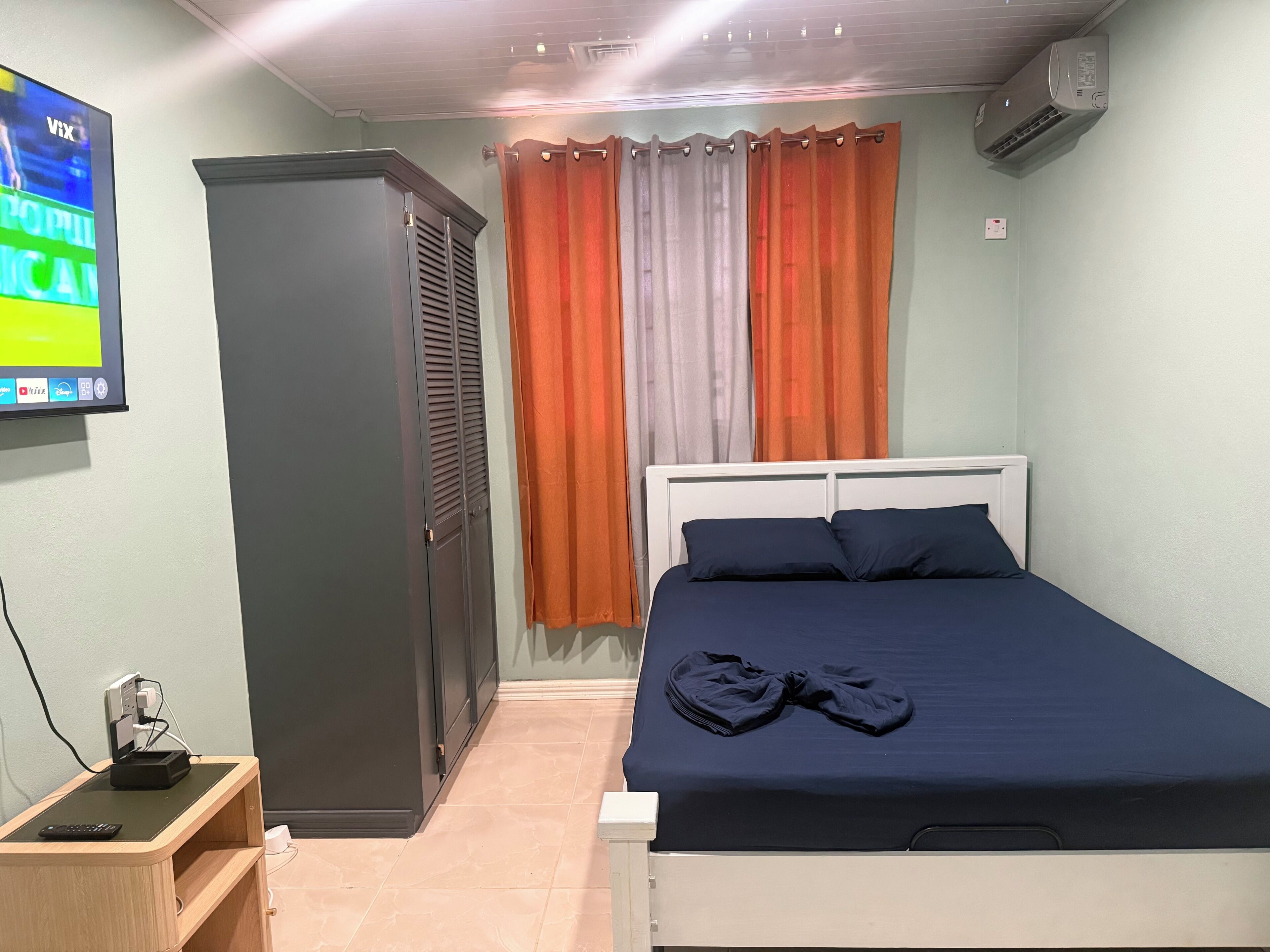 A bedroom with a bed, a wardrobe, a TV, and curtains.