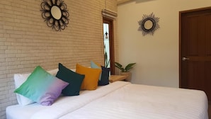 A bed with multiple pillows, a brick wall, a door, and a sunburst wall decoration.