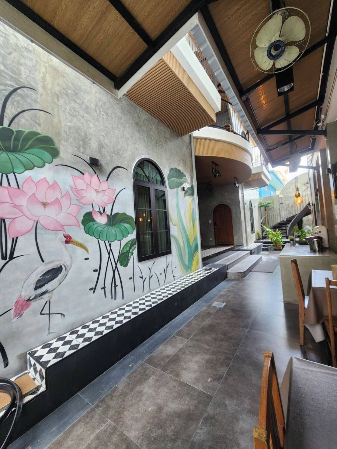 A restaurant with a mural of lotus flowers and a bird, a fan on the ceiling, and a checkered floor.