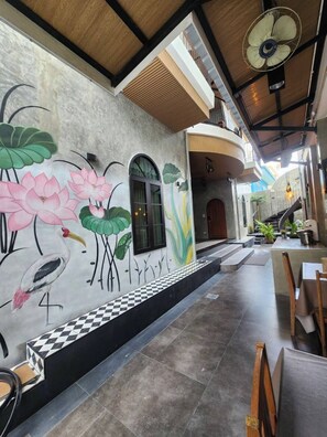 A restaurant with a mural of lotus flowers and a bird, a fan on the ceiling, and a checkered floor. - Baankorrakang (Bangkok)