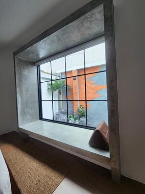 A room with a large window, a built-in bench, and a view of an outdoor brick wall. - Baankorrakang (Bangkok)