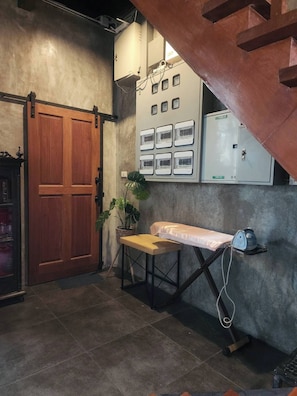 Une pièce avec une porte en bois, une petite table avec un banc, une plante en pot, un tableau électrique fixé au mur et un appareil fixé au plafond.