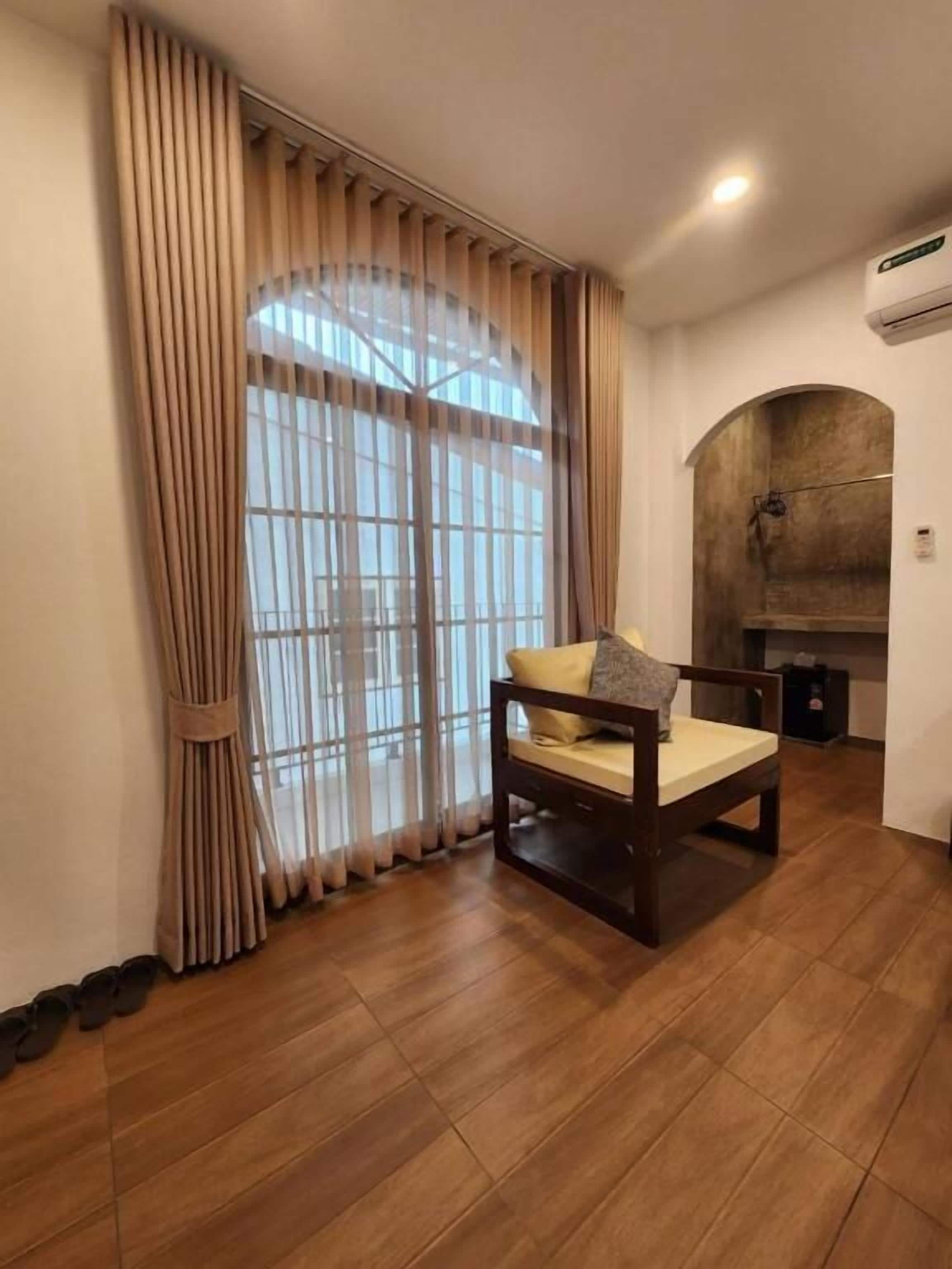 A room with a wooden floor, a bed with a pillow, a window with curtains, and a wall-mounted air conditioner.