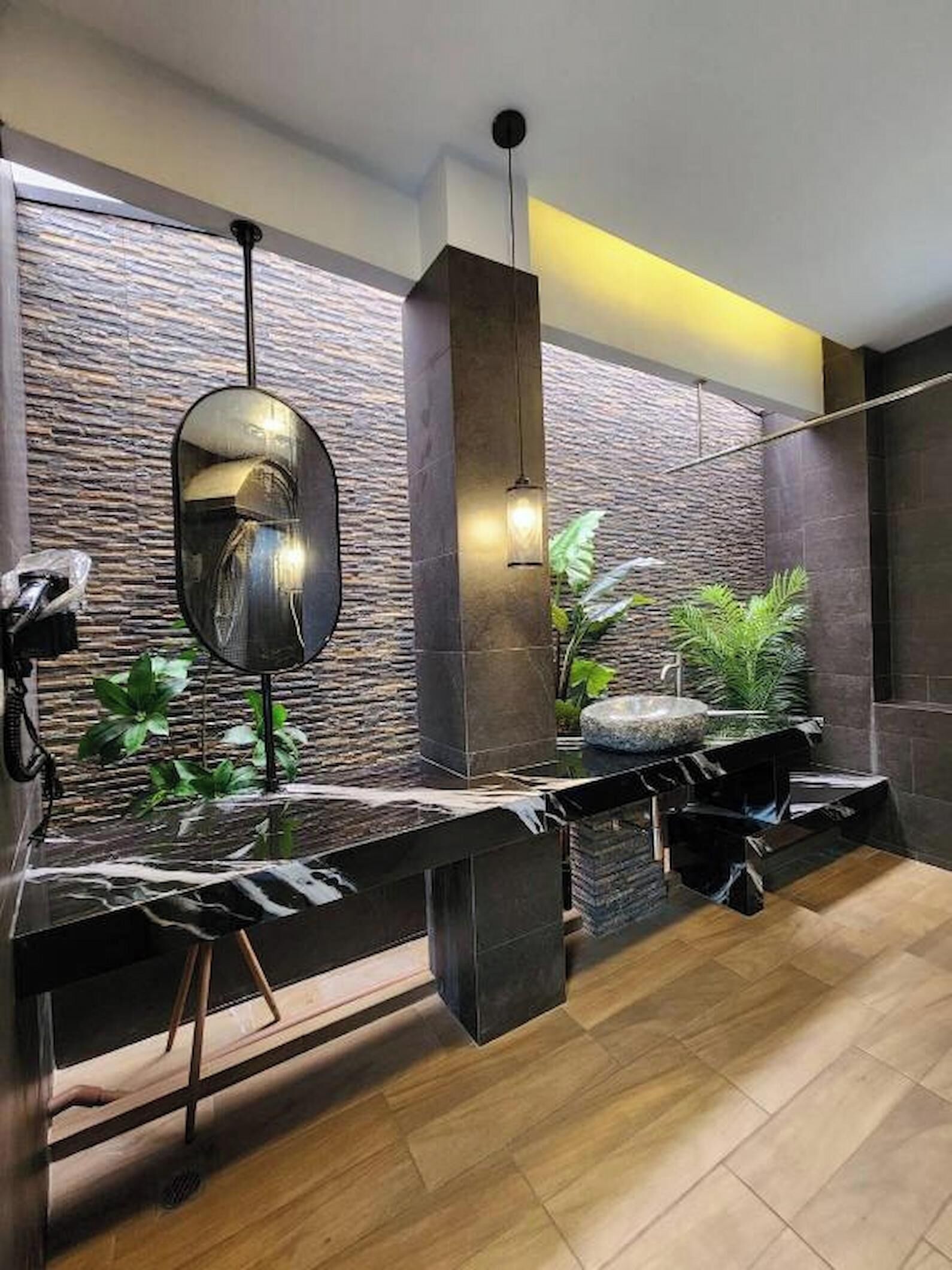 A modern bathroom with a stone wall, a round mirror, a sink, and a plant.