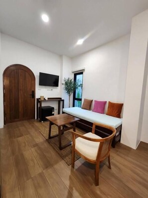 A living room with a sofa, a wooden table, a chair, a TV, and a door. - Baankorrakang (Bangkok)