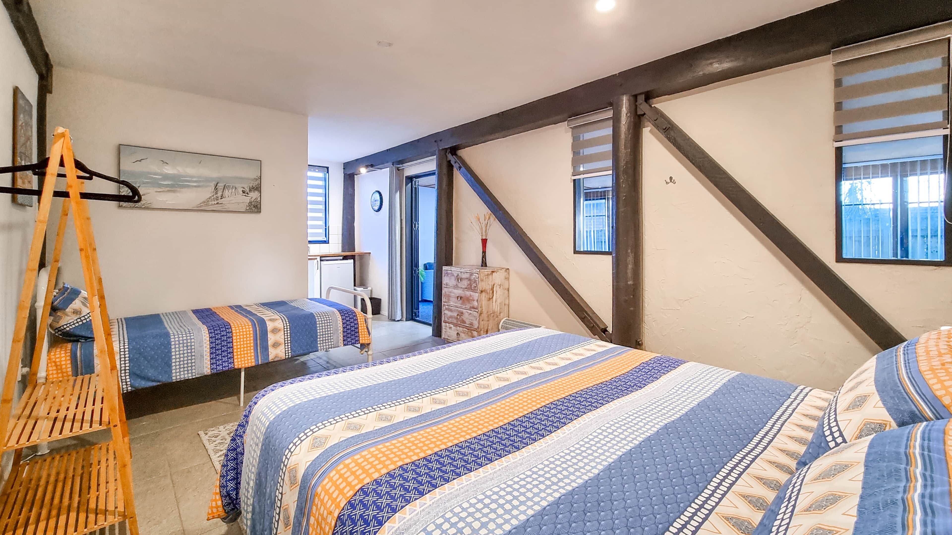 A bedroom with two beds, a wooden chair, a painting, and a view of the outside.