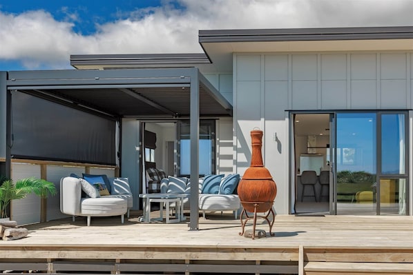 A modern outdoor patio with a covered seating area, a large terracotta pot, and a view into the house.