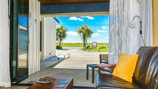 An open-plan living area with a view of a golf course, a leather sofa, a coffee table, and a lamp.