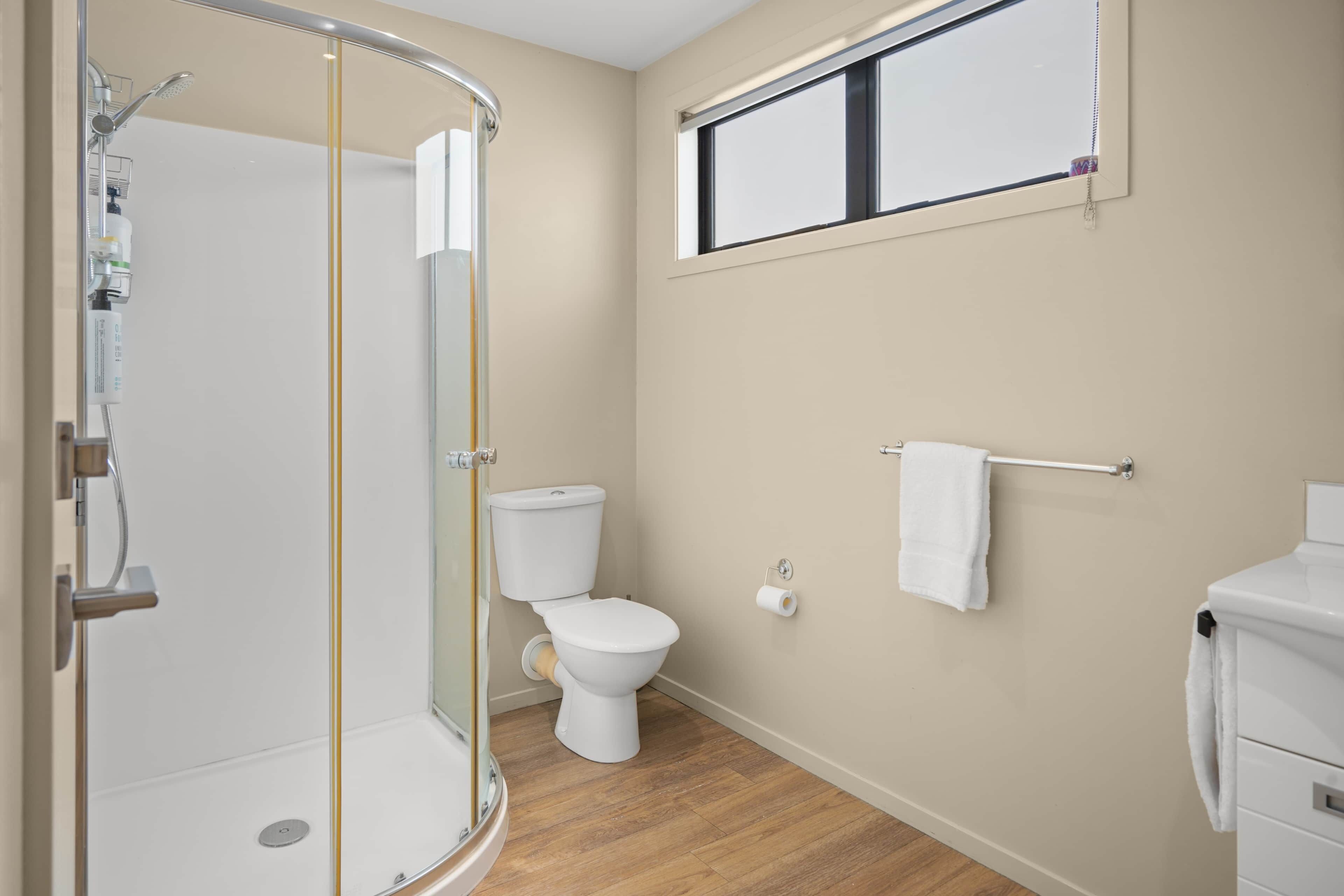 A bathroom with a glass-enclosed shower, a toilet, a towel rack, and a window.