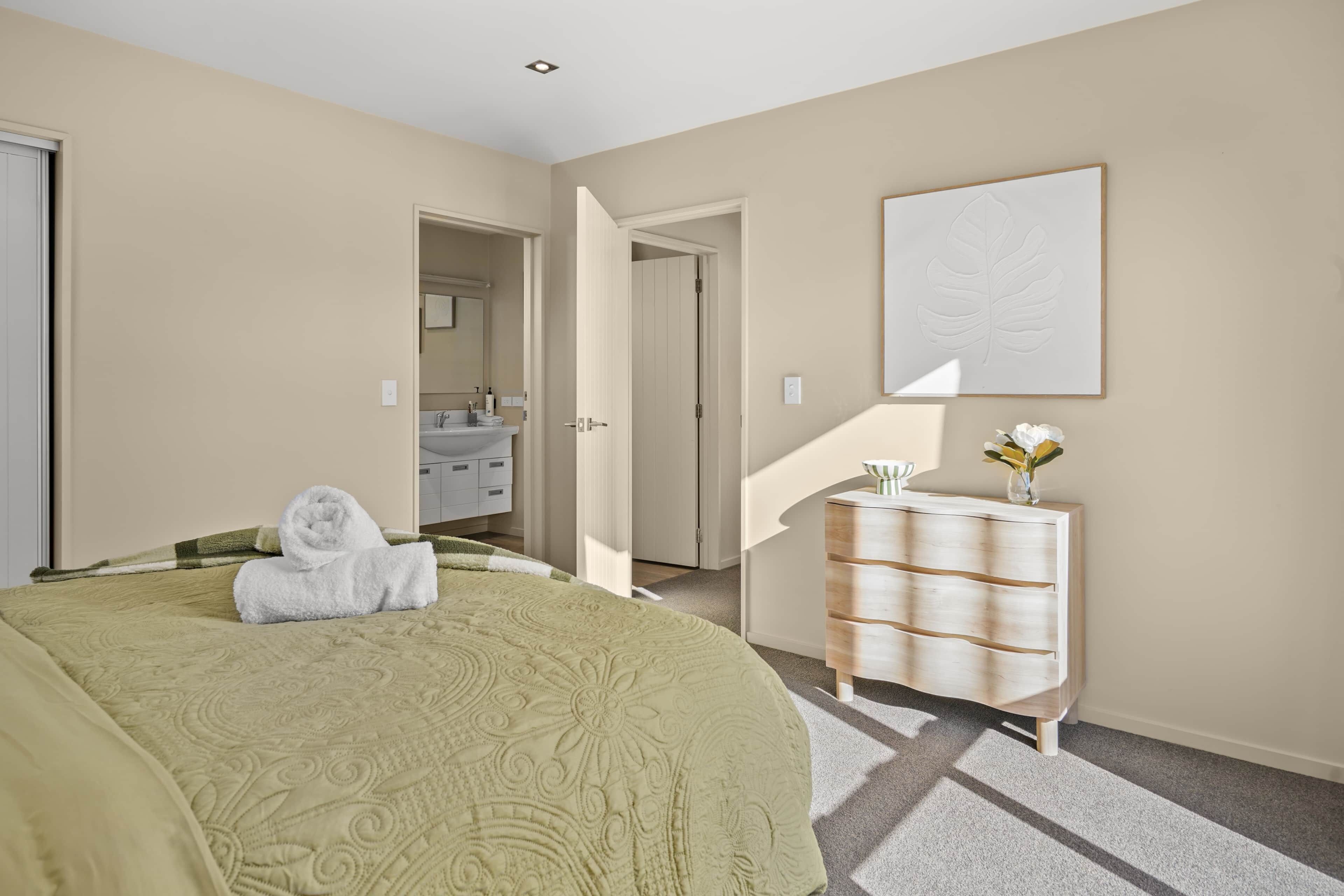 Un dormitorio con cama, cómoda, espejo y puerta que da a un baño.