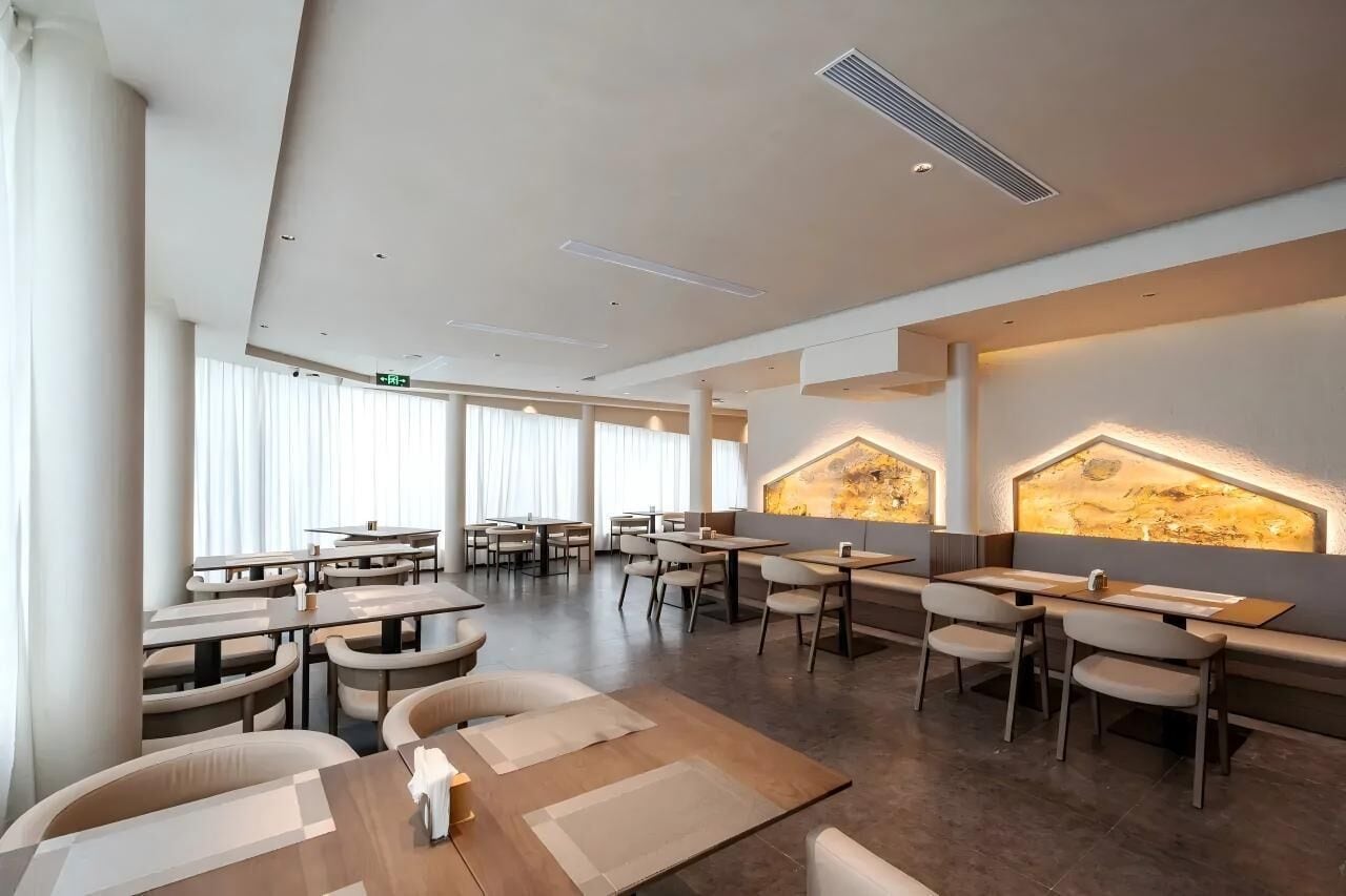 A modern restaurant with high ceilings, recessed lighting, and a central seating area with tables and chairs.