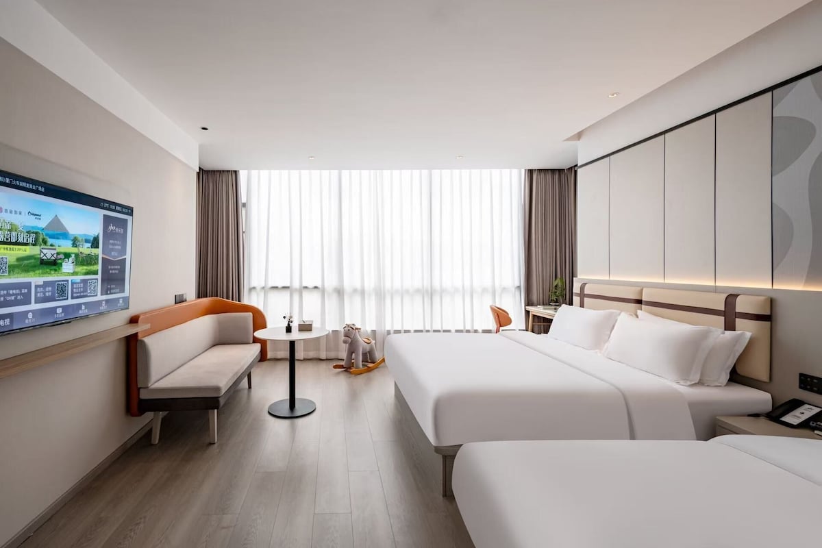 A hotel room with a bed, a sofa, a small table, and a TV on the wall.