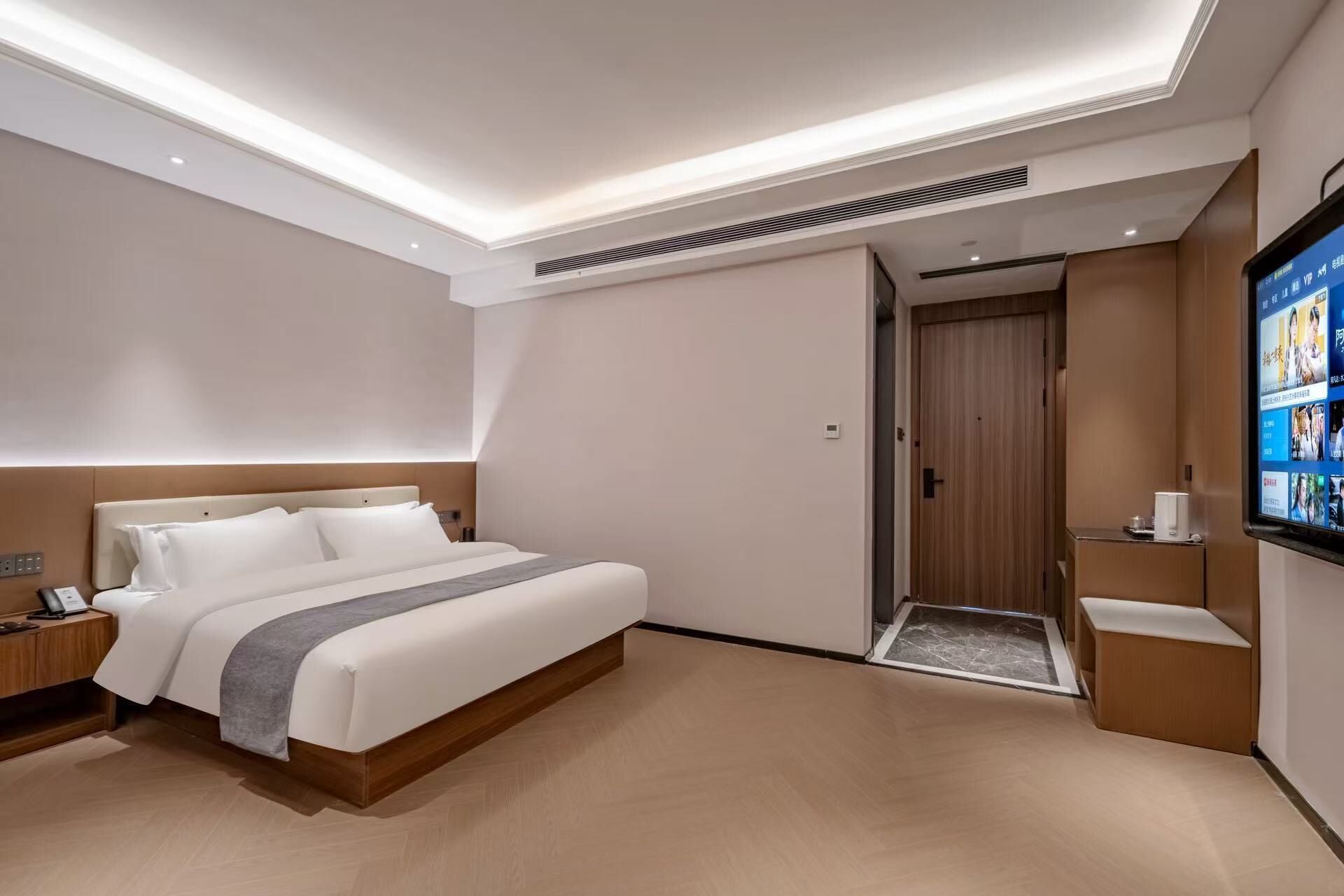 A modern hotel room with a large bed, a bedside table, a TV, and a door leading to a bathroom.