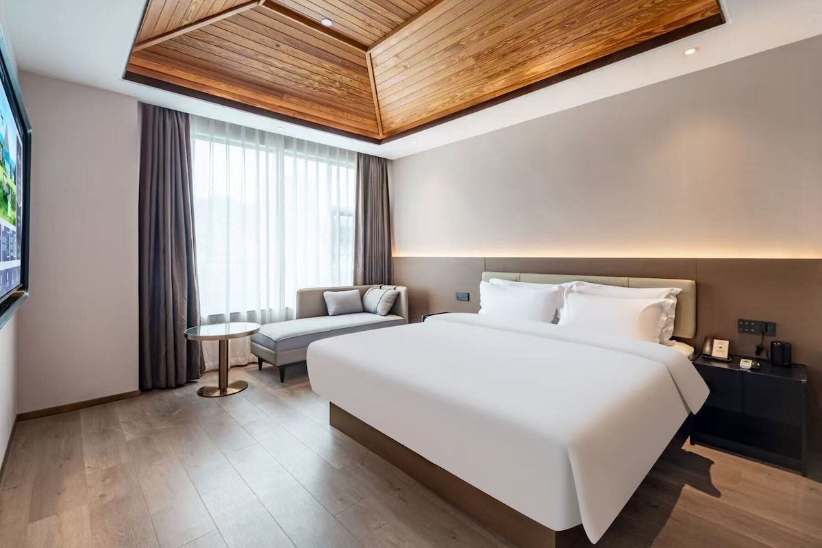 A modern hotel room with a large bed, a sofa, a small table, and a TV.