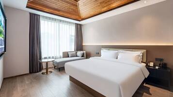 Una habitación de hotel moderna con una cama grande, un sofá, una mesita y un televisor.