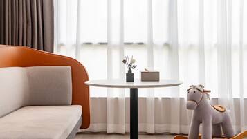 Una sala de estar moderna con un sofá, una mesa redonda, un caballito de madera y una ventana con cortinas translúcidas.