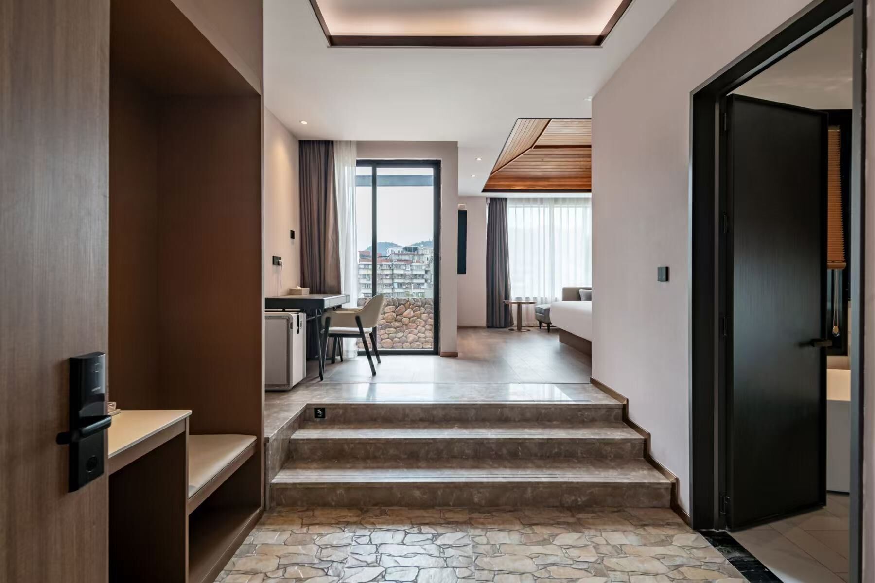 A modern hotel interior with a stone-tiled staircase leading to a balcony with a city view.